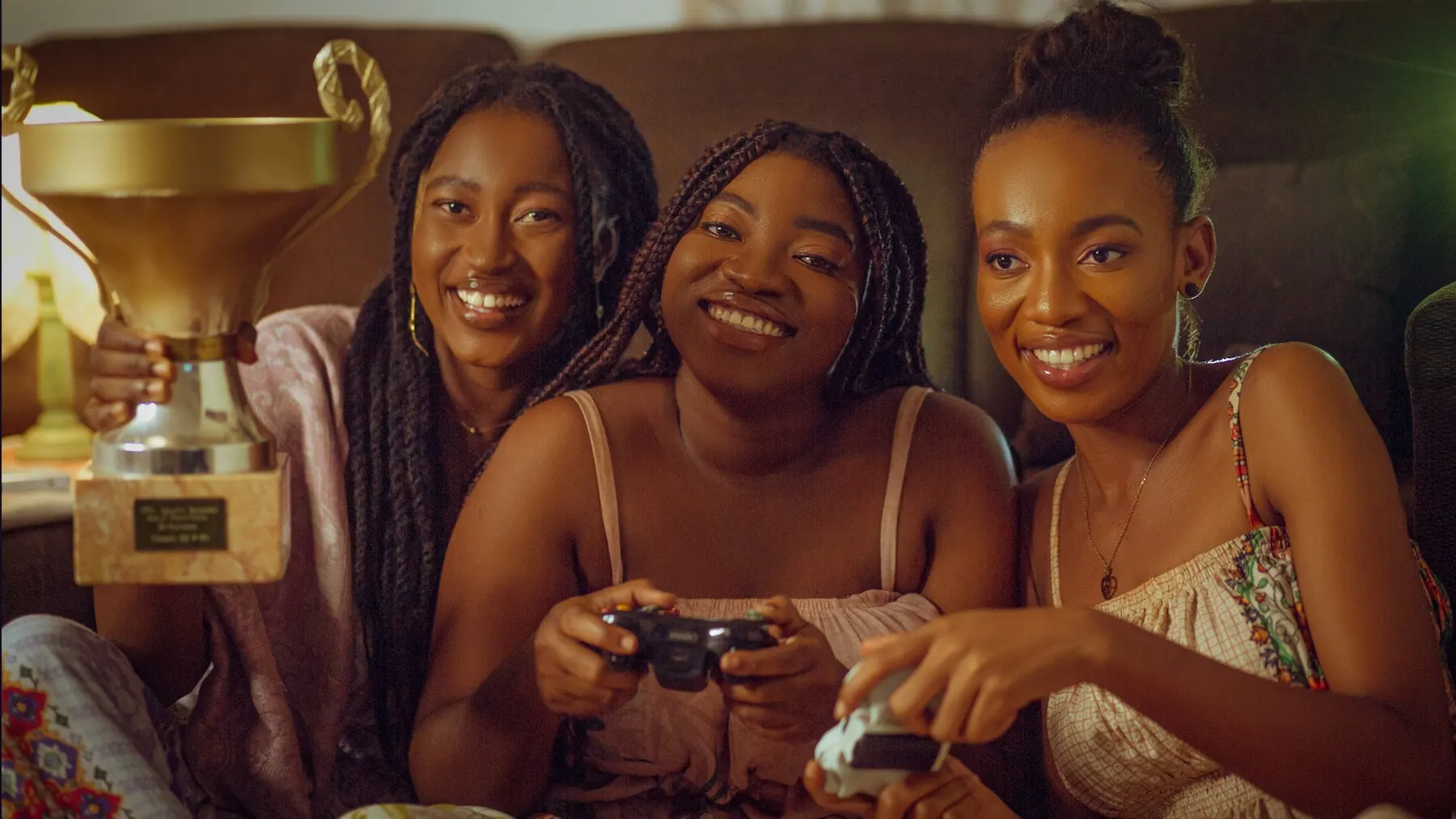 Three friends holding controllers and laughing beside a trophy
